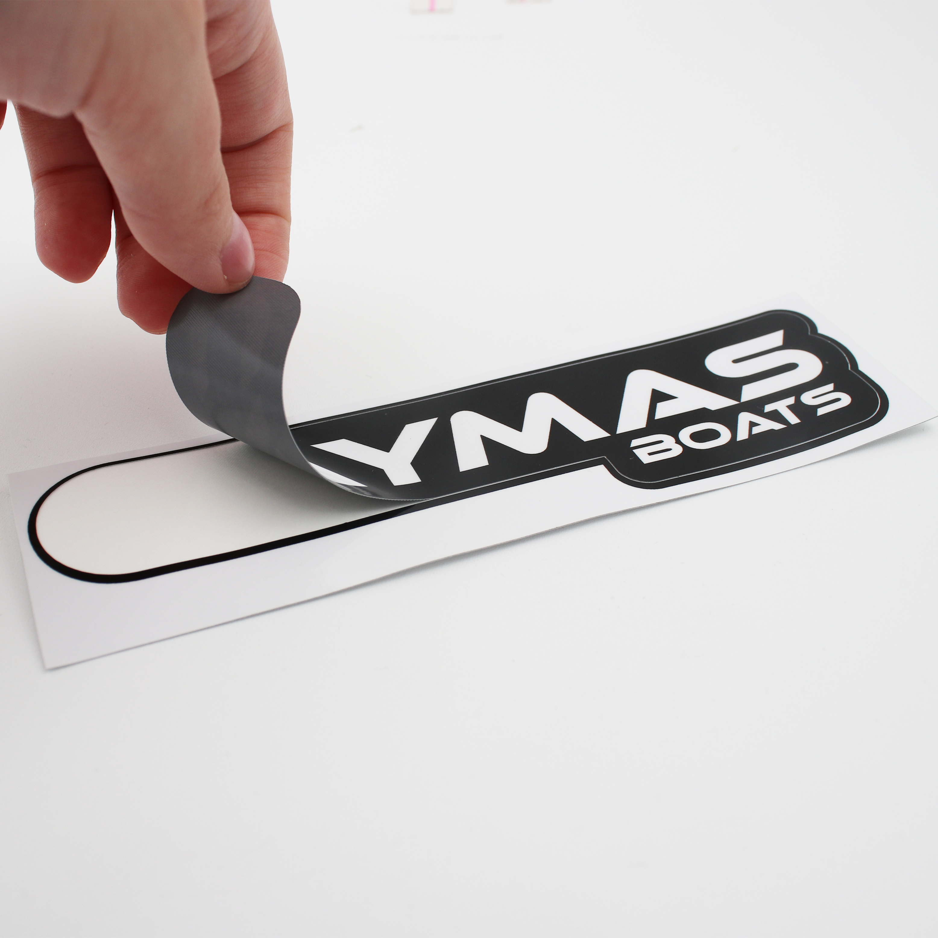 Hand pulling back a small black and white caymas boats logo decal from the background.