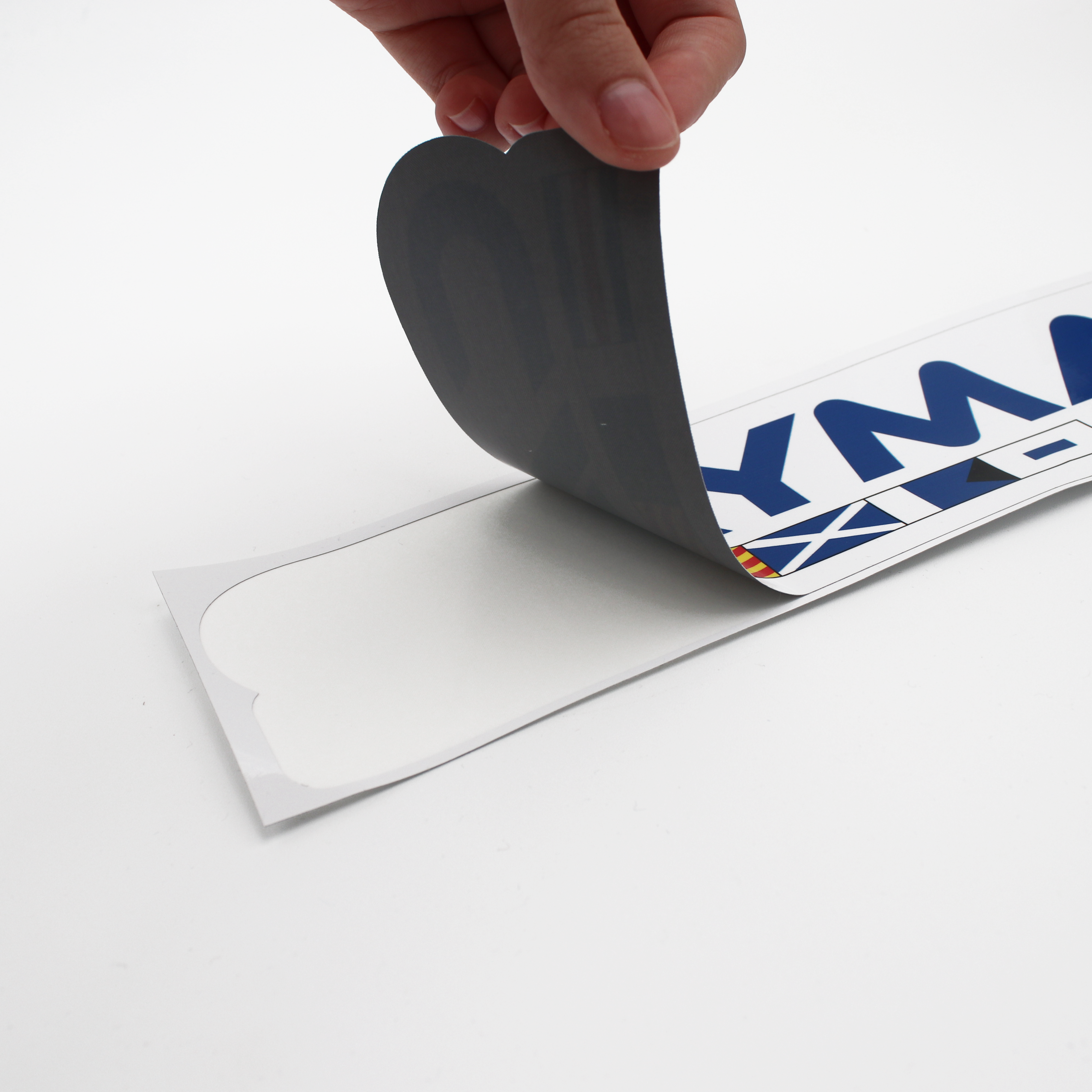 A hand pulling back a large colorful caymas boats logo decal from the transfer paper.
