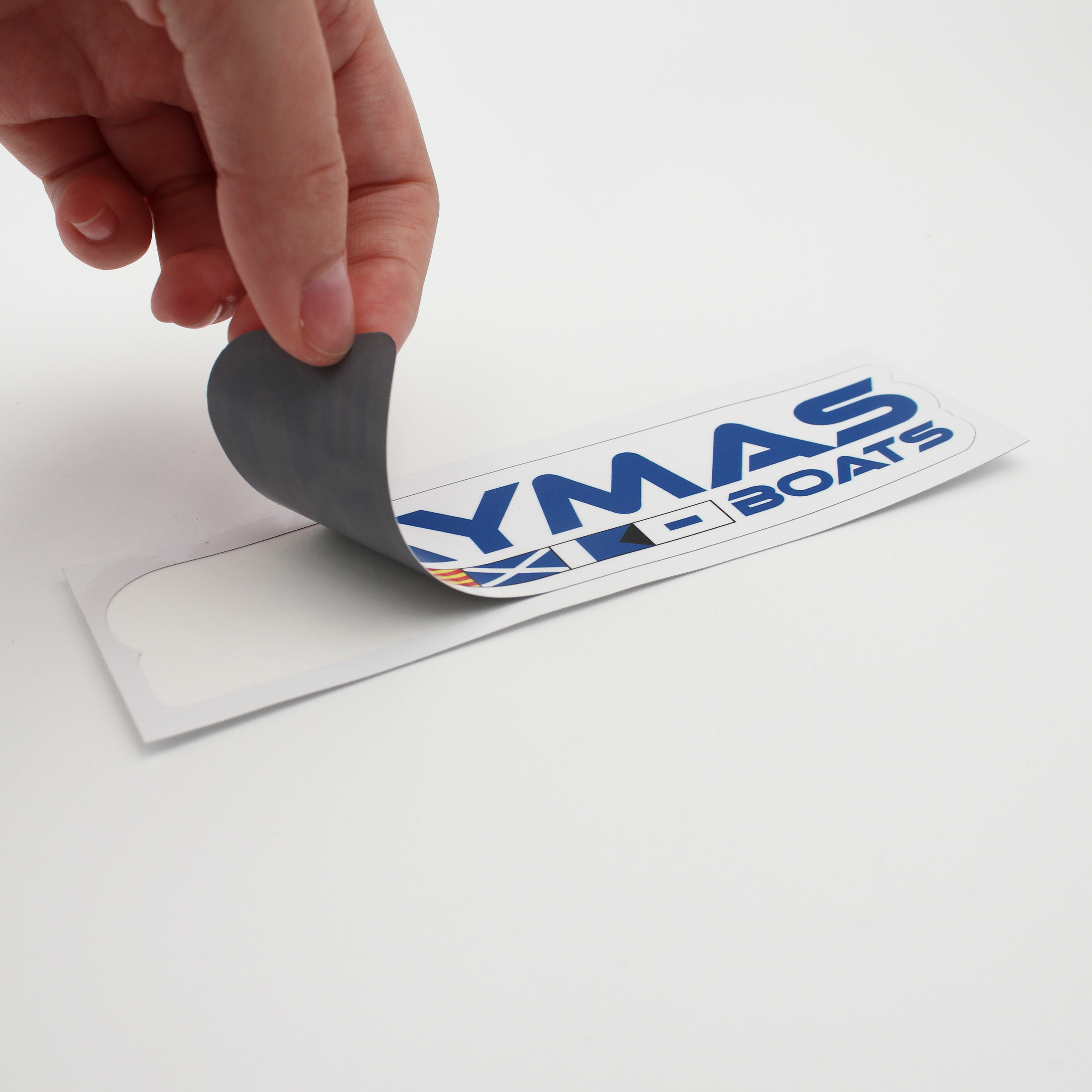 A hand pulling back a small colorful caymas boats logo decal from the transfer paper.
