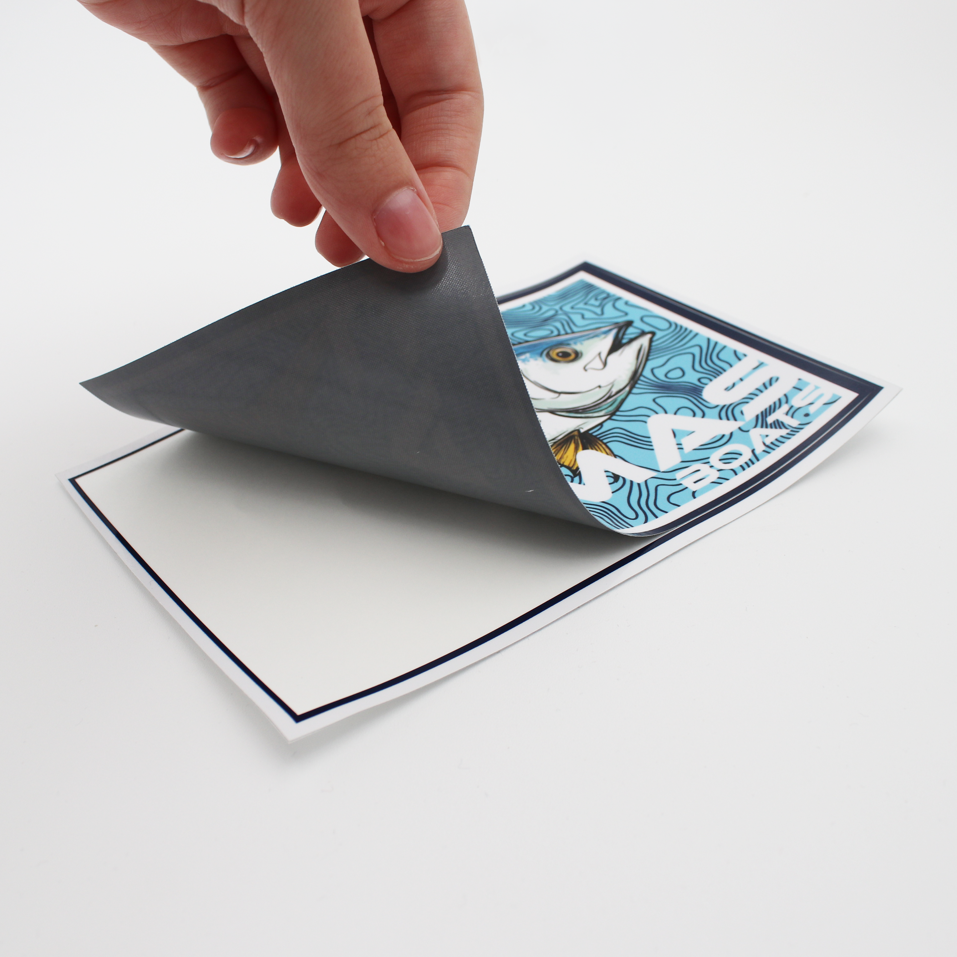 Hand peeling back a colorful decal of a blue and yellow fish with 'CAYMAS BOATS' branding.